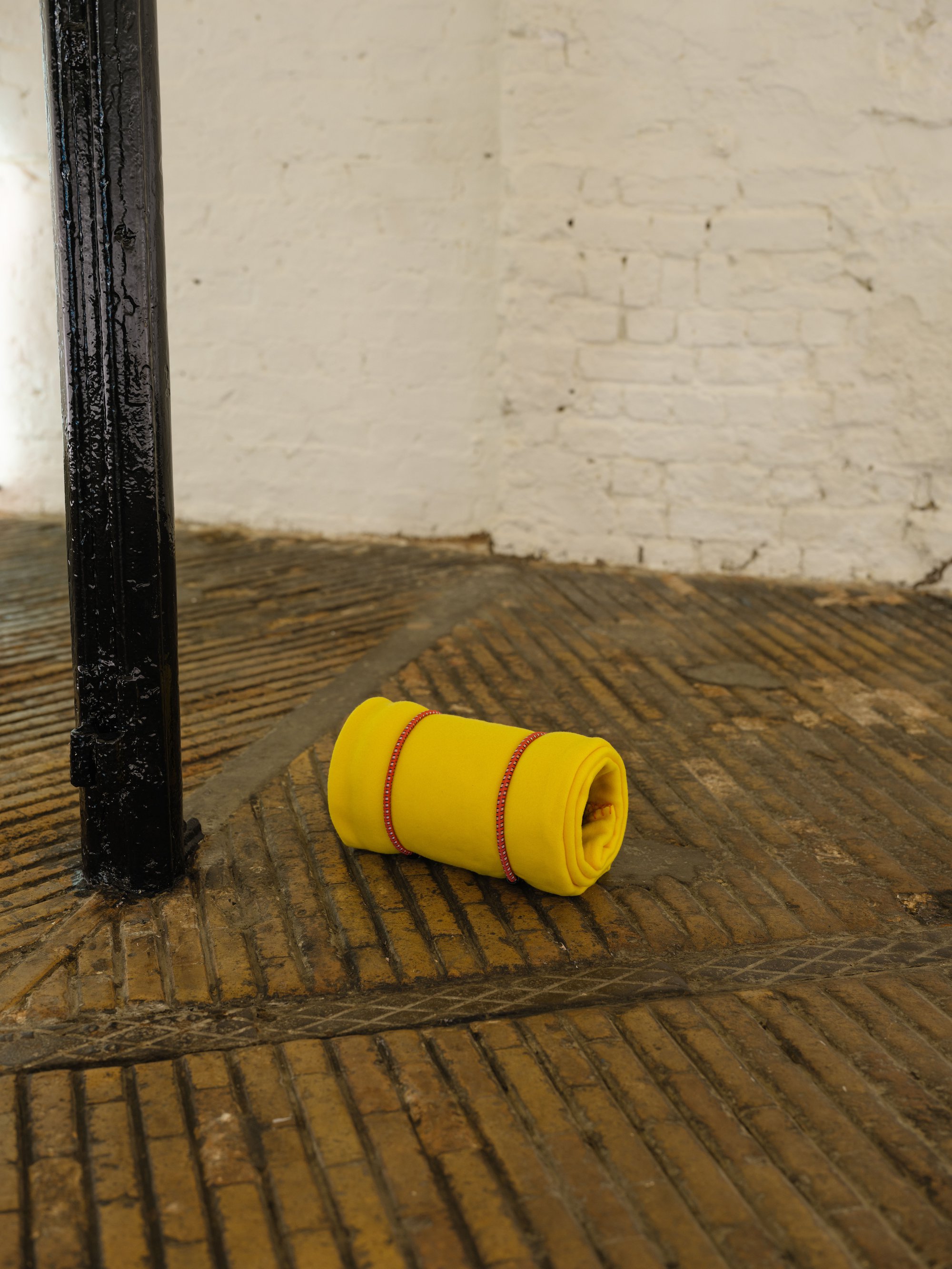 Liliana Moro, In No Time, Sound, 16 min. loop, wireless speaker, yellow blanket, red bungee cords, 19 x 18 x 32 cm (7 1/2 x 7 1/8 x 12 5/8 in), 2024. Installation view, In No Time, Rodeo, London, 2024