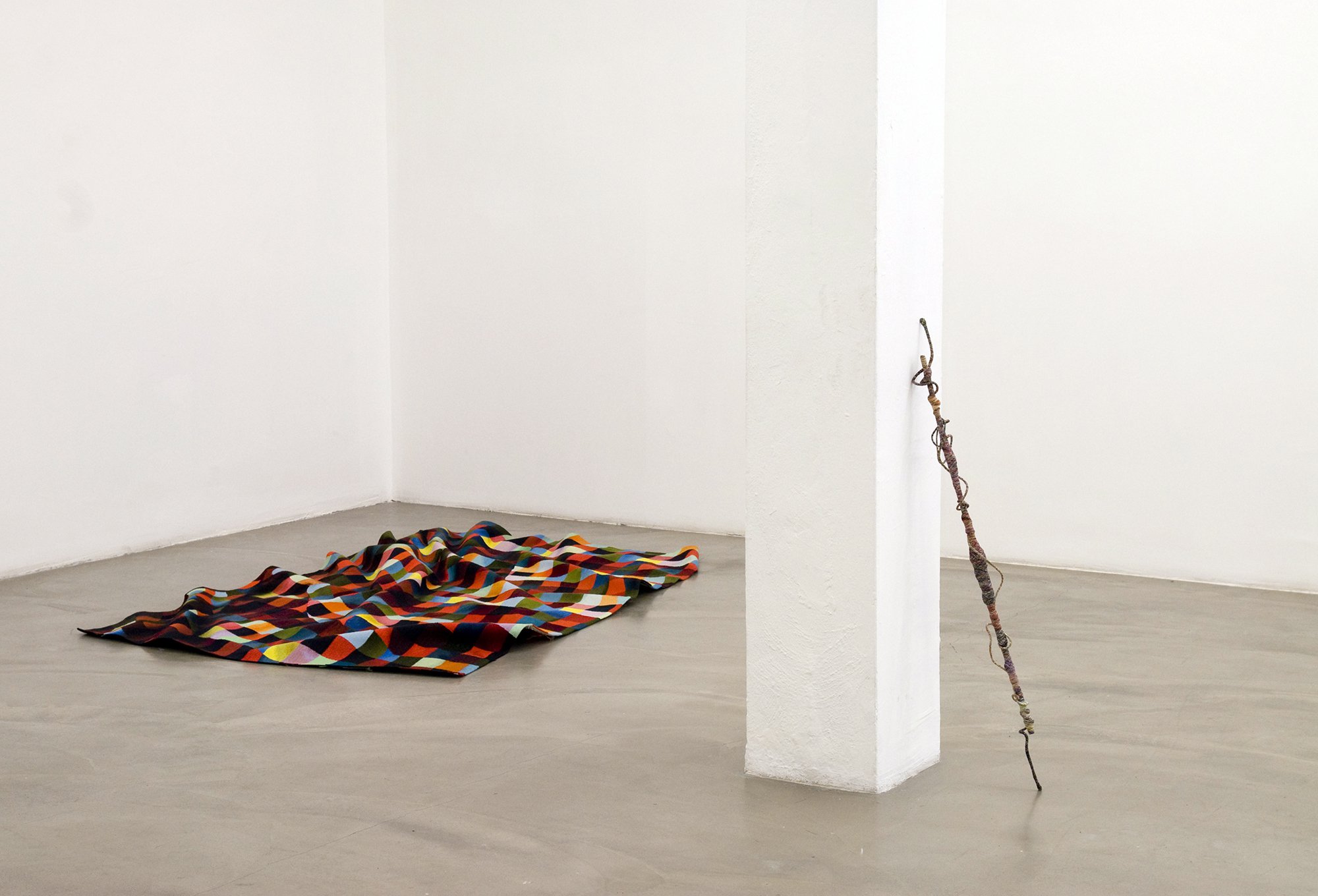 (Left) Rupert Norfolk, Pixelweave, Aubusson tapestry, 2005. (Right) Jim Lambie, Psychedelic Soul Stick 73, bamboo, wire, coloured thread, necklace, Ace of Spades playing card, green feather, Marlboro light packet, 105 x 8 x 8 cm (41 3/8 x 3 1/8 x 3 1/8 in), 2009. Installation view, Altogether Elsewhere, Rodeo, Istanbul, 2010